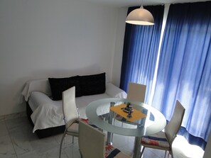 A hotel room with a bed, a round glass table with chairs, a hanging light fixture, and a window with blue curtains. - "Mir" mit Blick auf das Wasser by Interhome (Primošten)