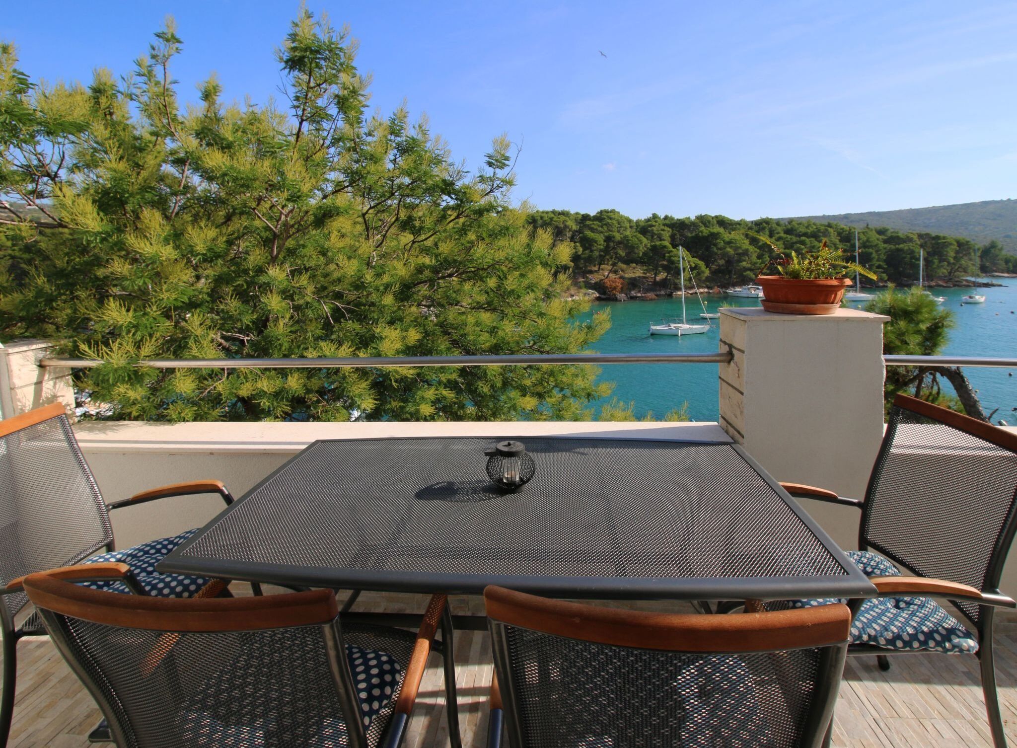 Una terraza con mesa y sillas, con vistas a un cuerpo de agua donde se ven botes y árboles.