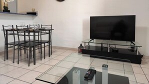 Ett modernt vardagsrum med ett matbord, stolar, en platt-TV på ett glasstativ, en väggklocka och en liten växt.