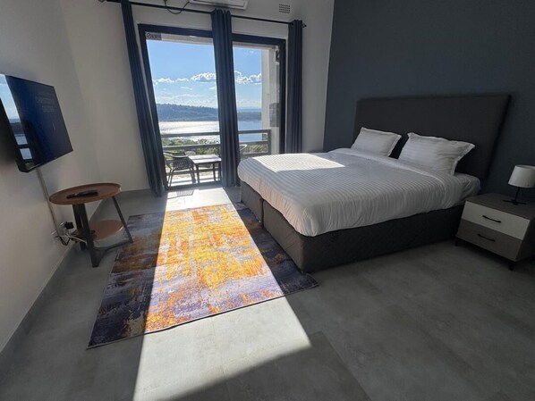 A modern bedroom with a large bed, a flat-screen TV, a small table, and a view of the outdoors.