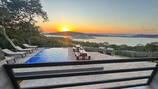 A pool area with lounge chairs and a table, overlooking a body of water and a sunset. - Apartment in siavonga (Siavonga)
