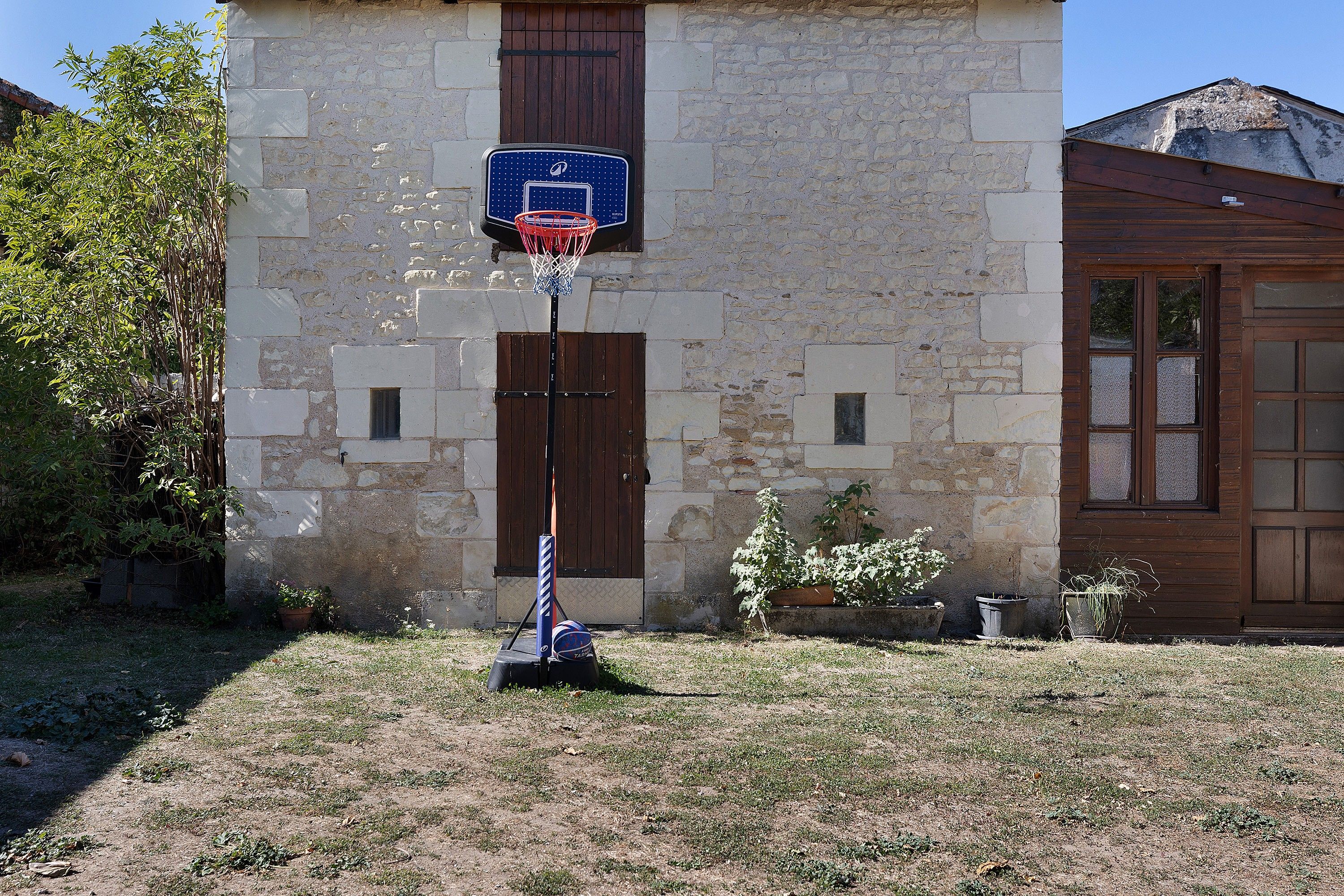 A basketball hoop installed on a stone wall with a wooden door and windows.