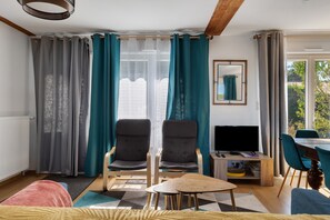 A modern living room with two armchairs, a small wooden table, a television, and a dining area with chairs.