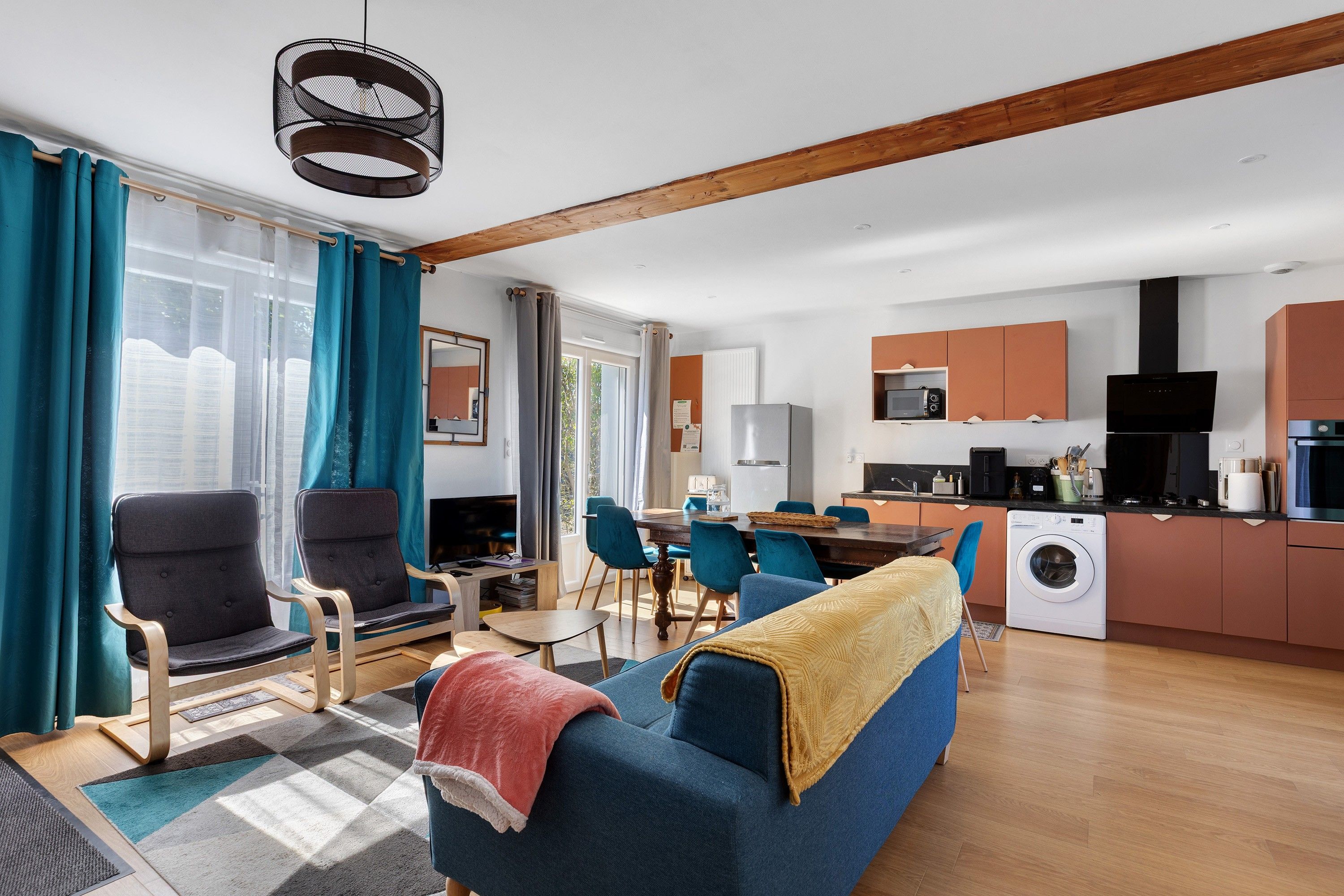 Een moderne woonkamer met een bank, stoelen en een eethoek. Er is een keuken met apparatuur en een wasmachine.
