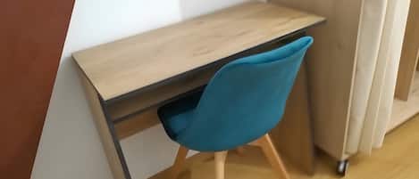 A corner desk with a blue chair, a wooden floor, and a white wall.