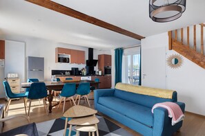 A modern living space with a dining area, kitchen, and a blue sofa.