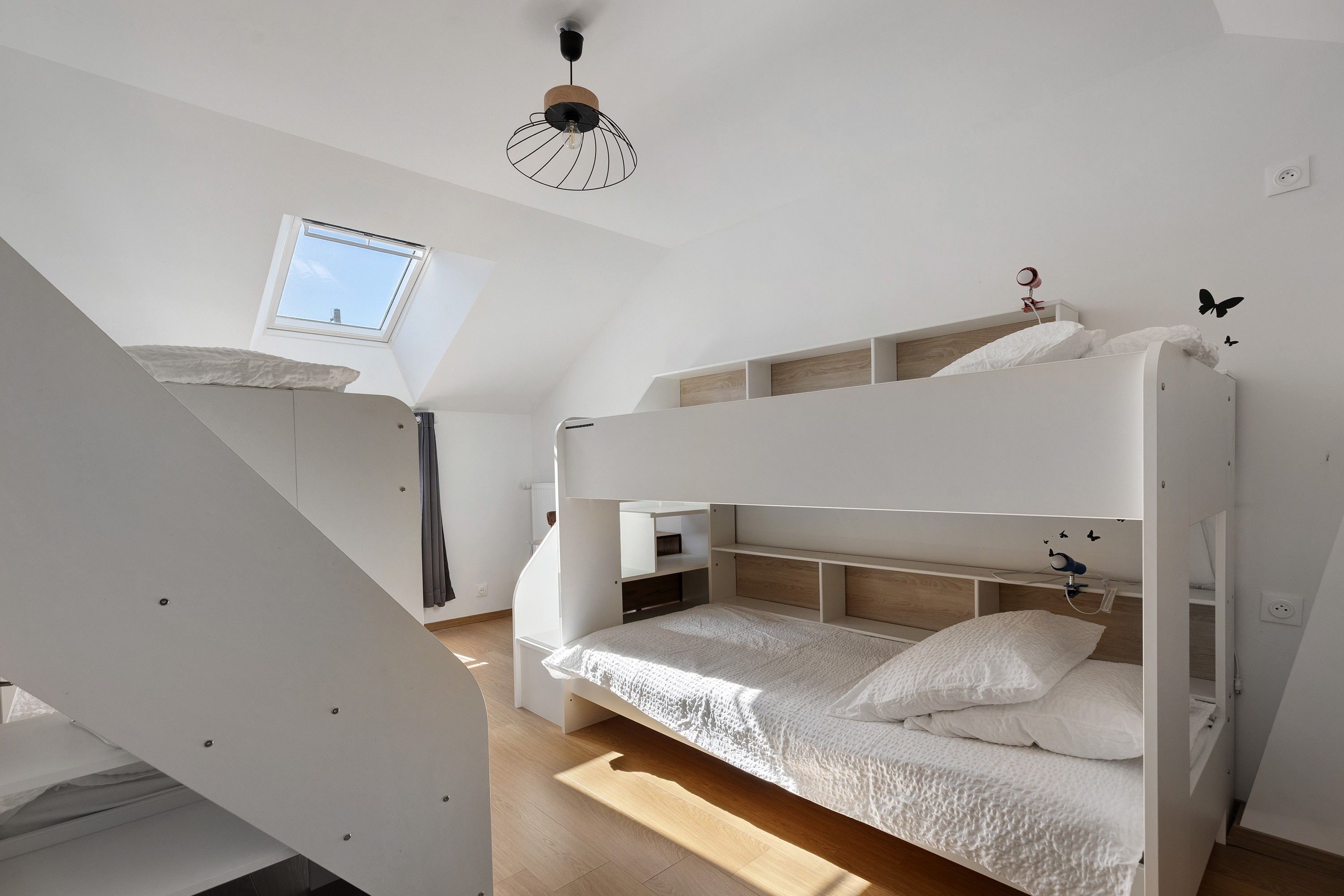 A bunk bed with a skylight and a ceiling fan in a room with a sloped ceiling.