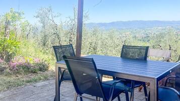 Eine Terrasse im Freien mit Tisch und Stühlen, einer Pergola darüber und Blick auf eine Landschaft mit Bäumen und Hügeln.
