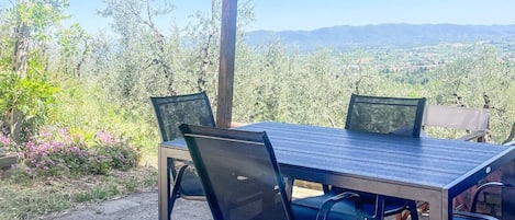 Une terrasse extérieure avec une table et des chaises, une pergola au-dessus et une vue sur un paysage arboré et vallonné.