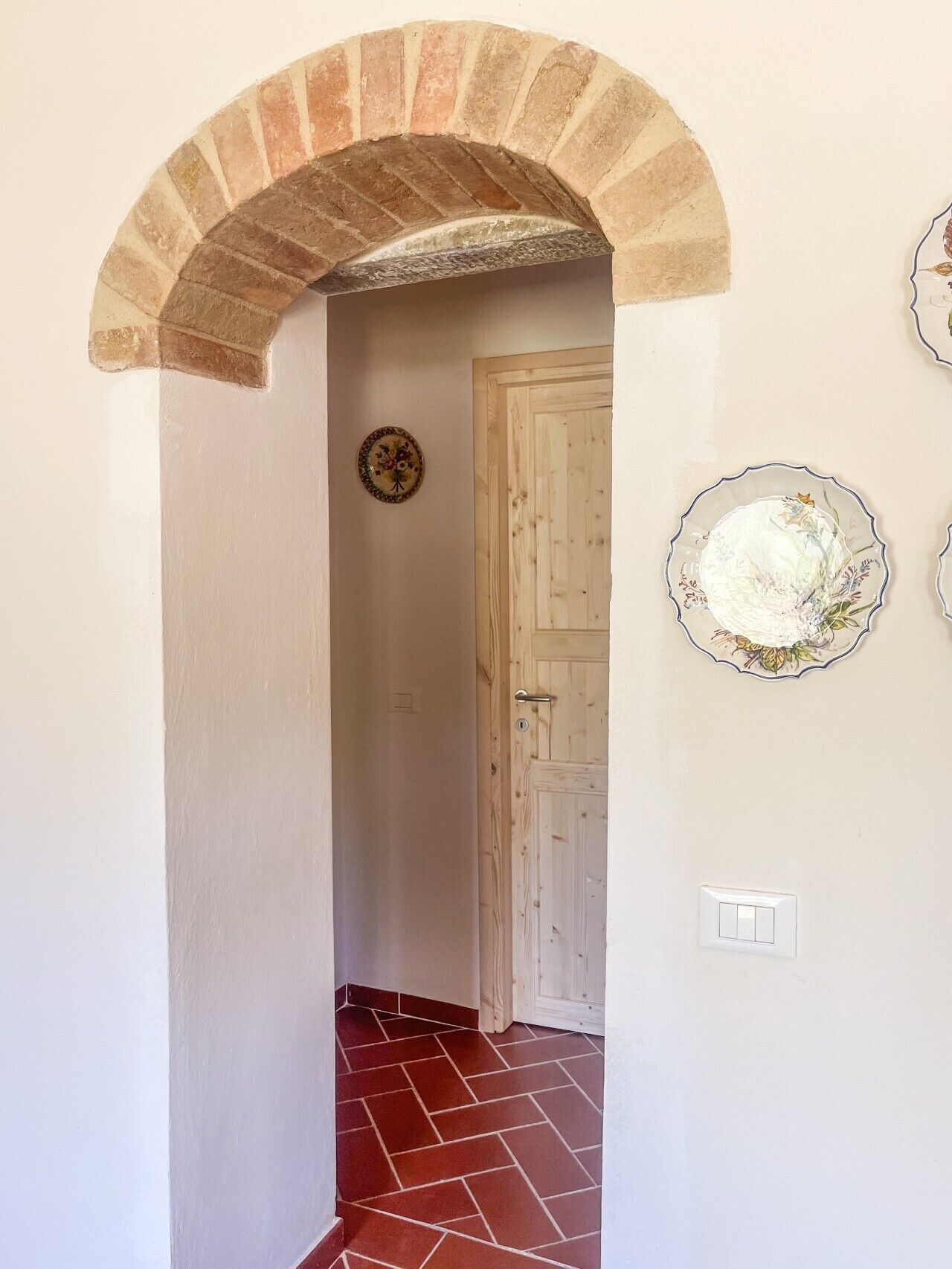 Un corridoio con un arco in mattoni, una porta in legno e due piastre decorative appese al muro.