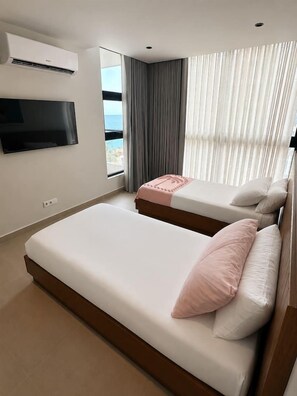 Une chambre d’hôtel avec deux lits, un téléviseur à écran plat fixé au mur et une grande fenêtre avec des rideaux.