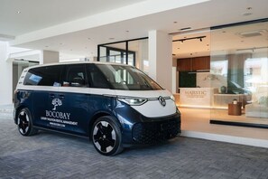 Ein kompakter Wagen mit der Aufschrift 'BOCOBAY LUXURY VACATION RENTAL MANAGEMENT' vor einem Gebäude mit Glasfassade und einem Schild, auf dem 'MAJESTIC APARTMENTS AND HOTEL' steht.