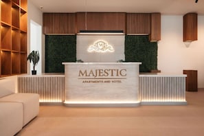 A reception desk with 'MAJESTIC APARTMENTS AND HOTEL' signage, wooden paneling, and a green wall with a decorative emblem. - Majestic 406 2-Bed Ocean View Suite by Bocobay (Willemstad)