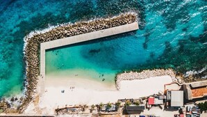 Vista aérea de uma área costeira com praia, um molhe rochoso e edifícios.