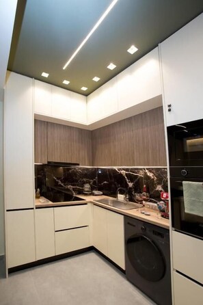 A compact kitchen with built-in appliances, a washing machine, and a microwave. - Luxury apartments near athens city center (Athina)