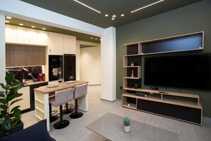 A modern kitchen with a dining area, a flat-screen TV mounted on the wall, and a potted plant. - Luxury apartments near athens city center (Athina)