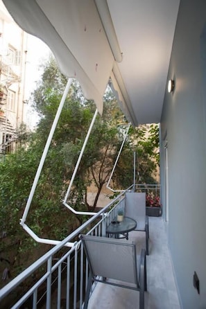 Un balcon avec une table et des chaises, une balustrade et une vue sur les arbres et les bâtiments.