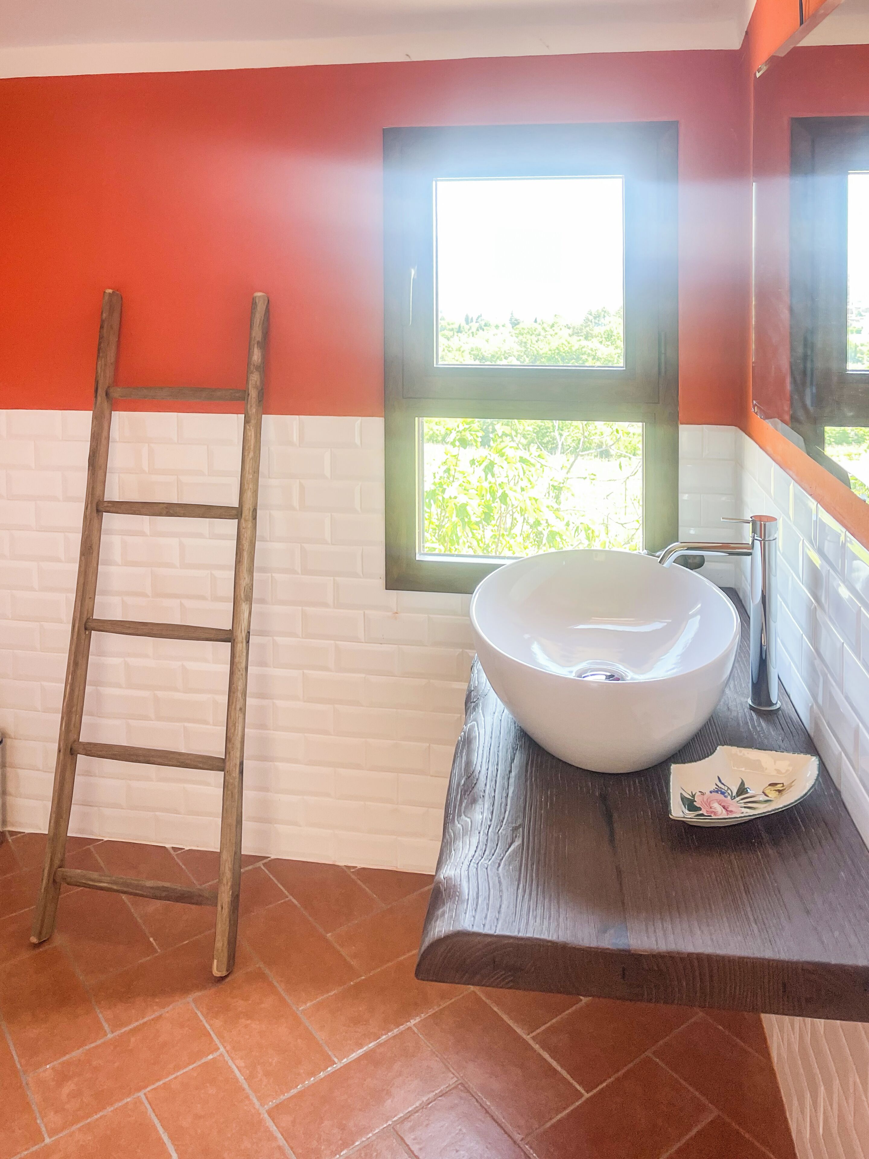 A bathroom with a white sink, a wooden ladder, and a window with a view of greenery.