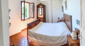 Une chambre à coucher avec un lit en bois, une table de chevet, un miroir et une fenêtre donnant sur un paysage verdoyant.