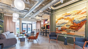 Een modern interieur met zitplaatsen, een groot wandtapijt en zichtbare ventilatiekanalen.