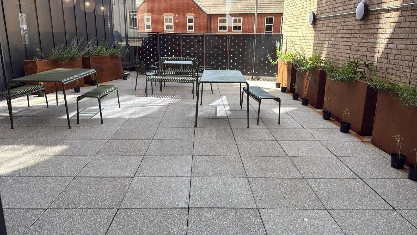 An outdoor patio area with a table and chairs, surrounded by potted plants and a brick wall.