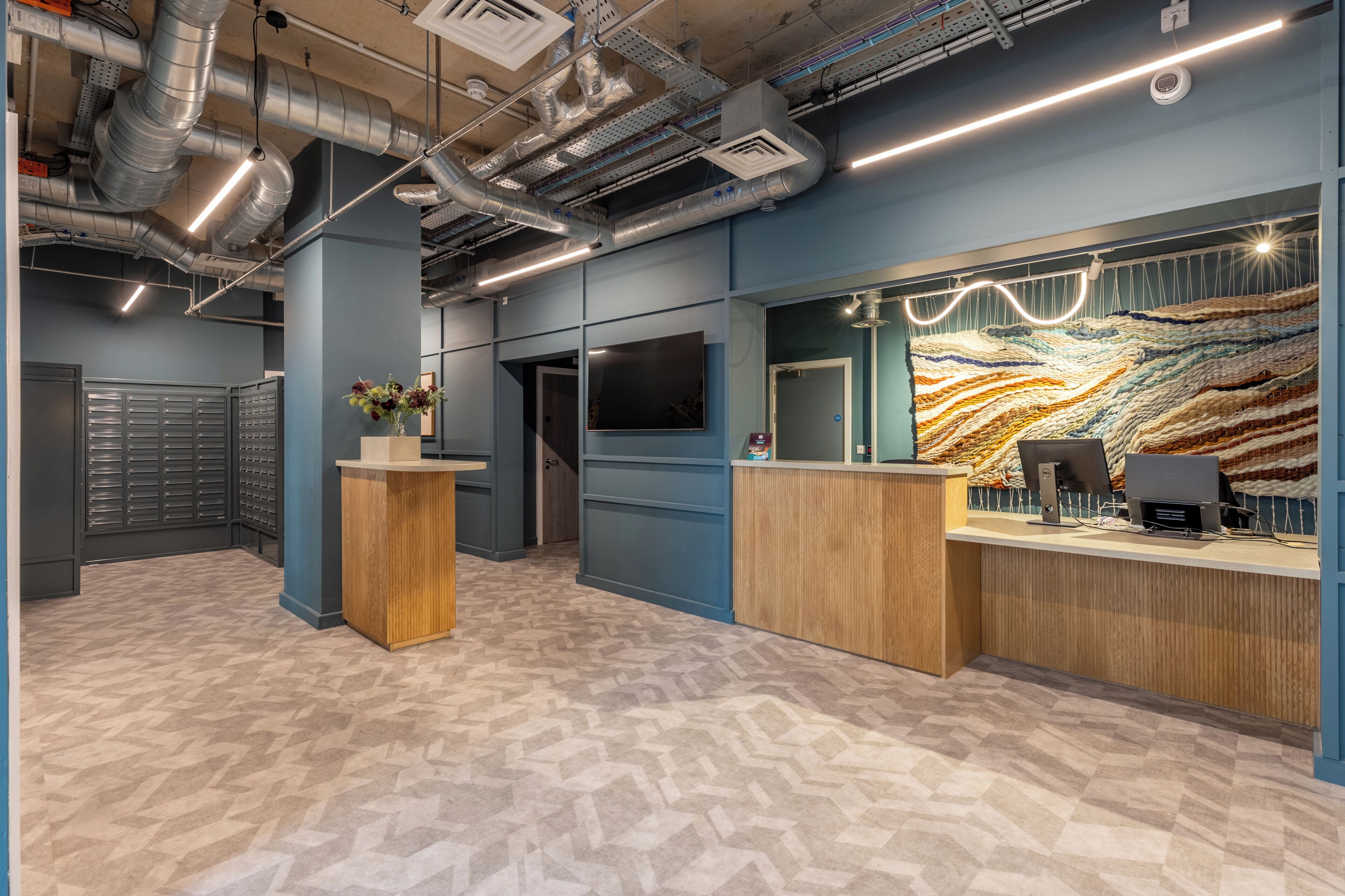 A reception area with a modern design, featuring a wooden reception desk, a large wall-mounted display, and a patterned floor.