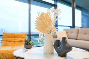 Ein modernes Wohnzimmer mit großem Fenster, rundem Couchtisch und einer Couch mit orangenen Kissen.