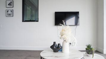 A modern living room with a white wall, a flat-screen TV mounted above a window, and two round tables with decorative vases.