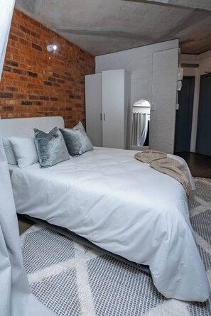 A bedroom with a brick wall, a bed with white bedding, and a wardrobe. - The 260 Collection Luxury City Apartment (Johannesburg)