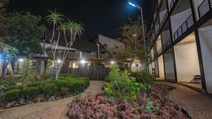 A courtyard with a paved walkway, various plants, and a building with multiple windows and balconies. - The 260 Collection Luxury City Apartment (Johannesburg)