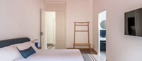 Un dormitorio con cama, mesita de noche, espejo y una puerta que da a otra habitación.