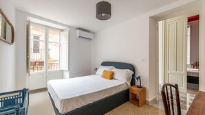 Et soveværelse med seng, natbord, lampe, stol og en aircondition.
