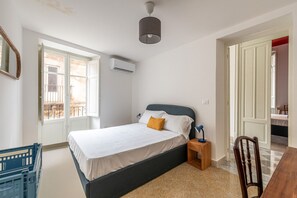 Ein Schlafzimmer mit Bett, Nachttisch, Lampe, Stuhl und Klimaanlage.
