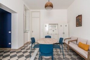 Ein gemütlicher, kleiner Wohnbereich mit rundem Tisch, blauen Stühlen, einer Couch und einer Küchenzeile.
