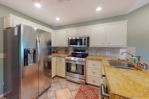 A modern kitchen with stainless steel appliances, white cabinetry, and a granite countertop. - Lake Travis Waterfront Home with Dock Access | 4BR (Lakeway)