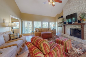A living room with a fireplace, sofas, a television, and a ceiling fan. - Lake Travis Waterfront Home with Dock Access | 4BR (Lakeway)