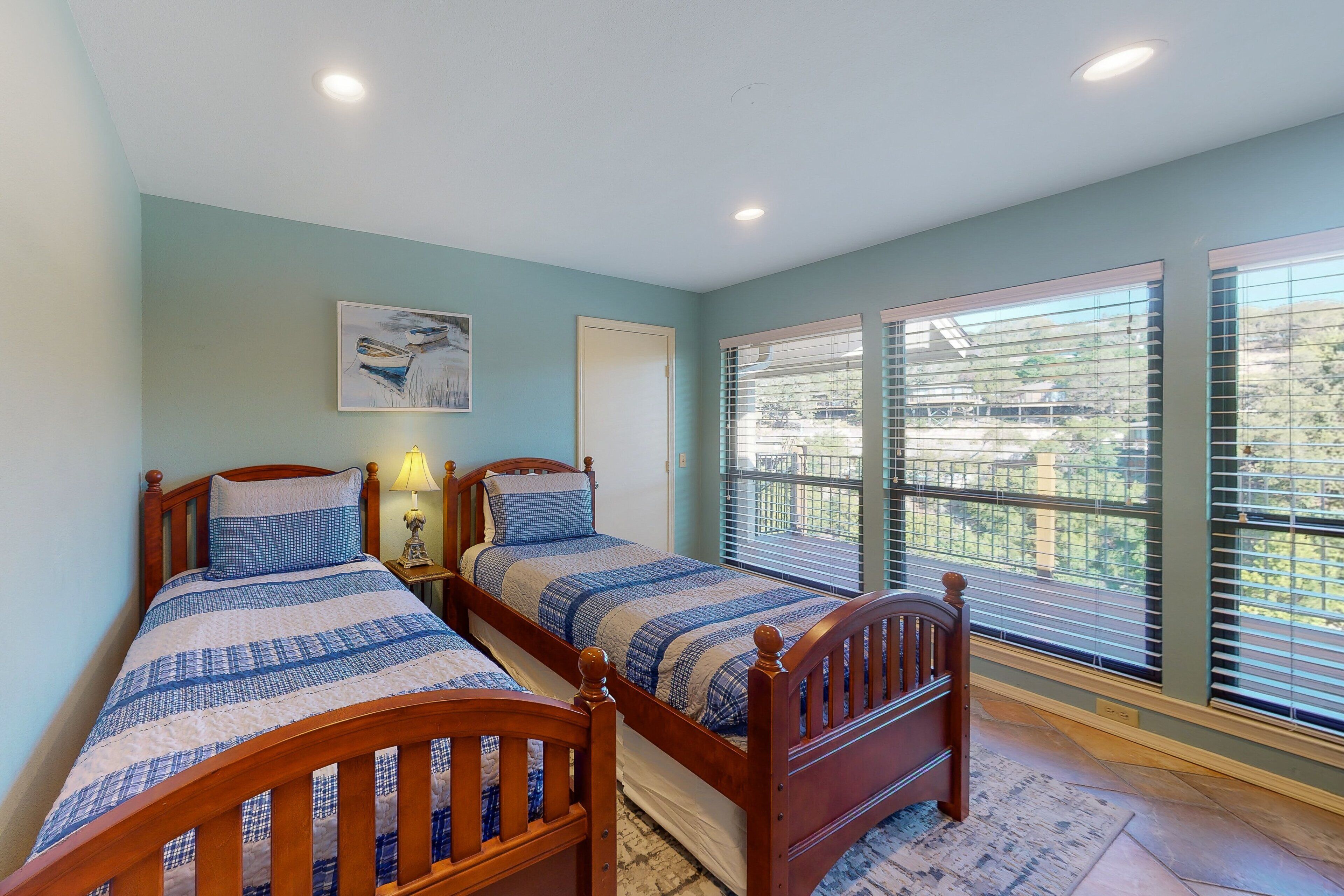 A bedroom with two wooden beds, a painting on the wall, and a window with blinds.