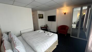 Une chambre d’hôtel avec un lit, une télévision, un fauteuil rouge et une porte coulissante donnant sur une salle de bain.