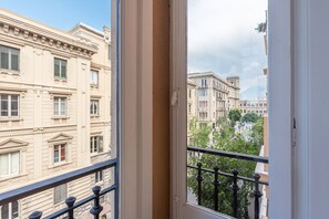 Blick von einem Balkon mit Metallgeländer auf eine Straße mit historischen Gebäuden.