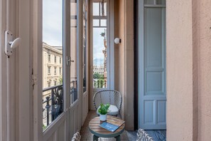 A balcony with a wicker chair, a small table with a plant and a book, and a view of buildings. - Roma 1923 - Casa Verde by Wonderful Italy (Palermo)