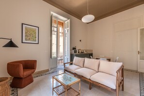 Ein Wohnzimmer mit einer Couch, einem kleinen Tisch, einem Sessel, einer Lampe und einem Bild an der Wand.