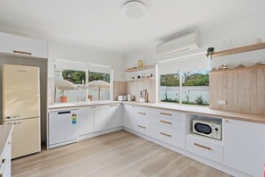 A modern kitchen with white cabinetry, a built-in dishwasher, and a microwave. - Mediterranean Beachside retreat with a pool (Broadwater)