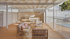 Un patio al aire libre con piscina, mobiliario cubierto y un cerramiento decorativo.
