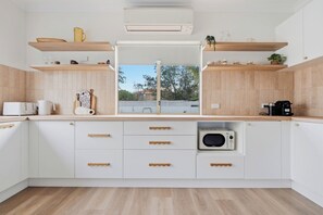 A modern kitchen with white cabinetry, wooden countertops, a built-in microwave, and a window with a view of the outside. - Mediterranean Beachside retreat with a pool (Broadwater)