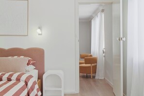 A bedroom with a bed, a chair, and a door leading to another room. - Mediterranean Beachside retreat with a pool (Broadwater)
