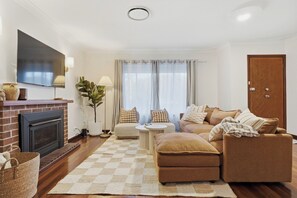 A living room with a fireplace, sofa, and a television mounted on the wall. - Mediterranean Beachside retreat with a pool (Broadwater)