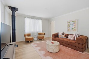 A living room with a sofa, two armchairs, a coffee table, a TV, and a fireplace. - Mediterranean Beachside retreat with a pool (Broadwater)