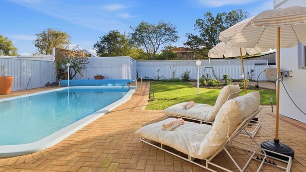 Un patio trasero con piscina, sillones de descanso y un área de patio techada.