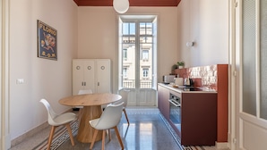 Eine kleine Küche mit Essbereich, einem weißen Schrank, einem runden Holztisch und Blick durch eine Glastür.
