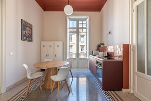 A compact kitchen with a dining area, a white cabinet, a round wooden table, and a view through a glass door. - Roma 1923 - Casa Rossa by Wonderful Italy (Palermo)